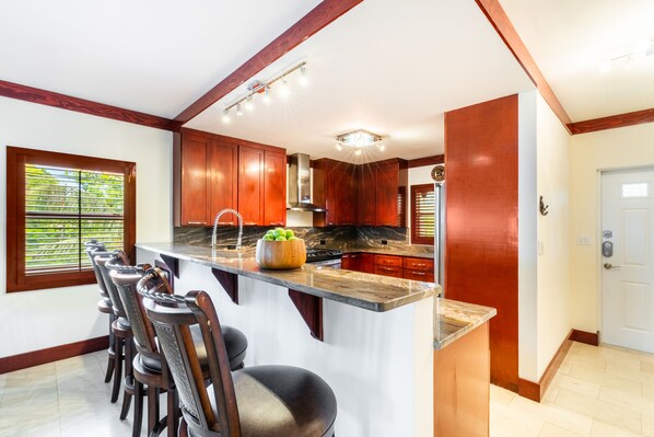 A kitchen with wooden cabinets, a large island with bar stools, and a window with blinds.
