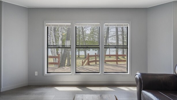 Una habitación con tres ventanas amplias, piso de madera y un sofá de cuero.