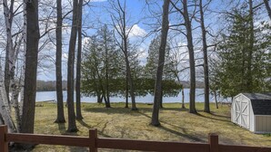 Vista de un lago con altos árboles, un área verde y un cobertizo pequeño.