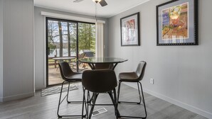 Un comedor moderno con una mesa de vidrio, cuatro sillas, un ventilador de techo y dos obras de arte enmarcadas en la pared.