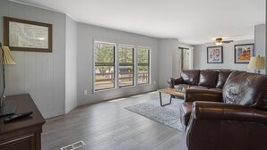 Amplia sala de estar con un sofá de cuero marrón, una mesa de centro de madera y vistas a una terraza exterior a través de amplios ventanales.