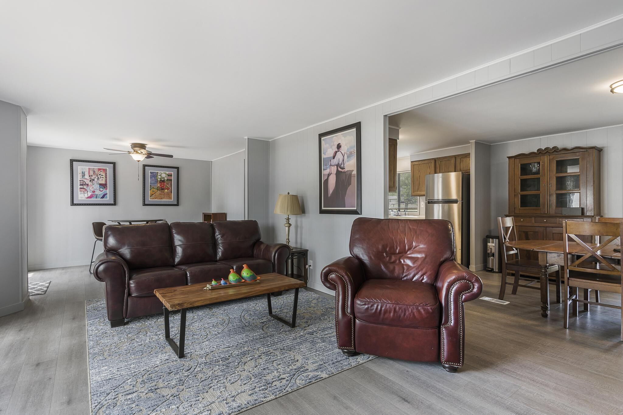 Una sala moderna con un sofá de cuero marrón, una mesa de centro de madera y un comedor con mesa y sillas de madera.