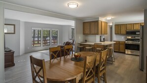 Una cocina amplia con armarios de madera, un comedor con mesa y sillas de madera, y vistas por grandes ventanales.