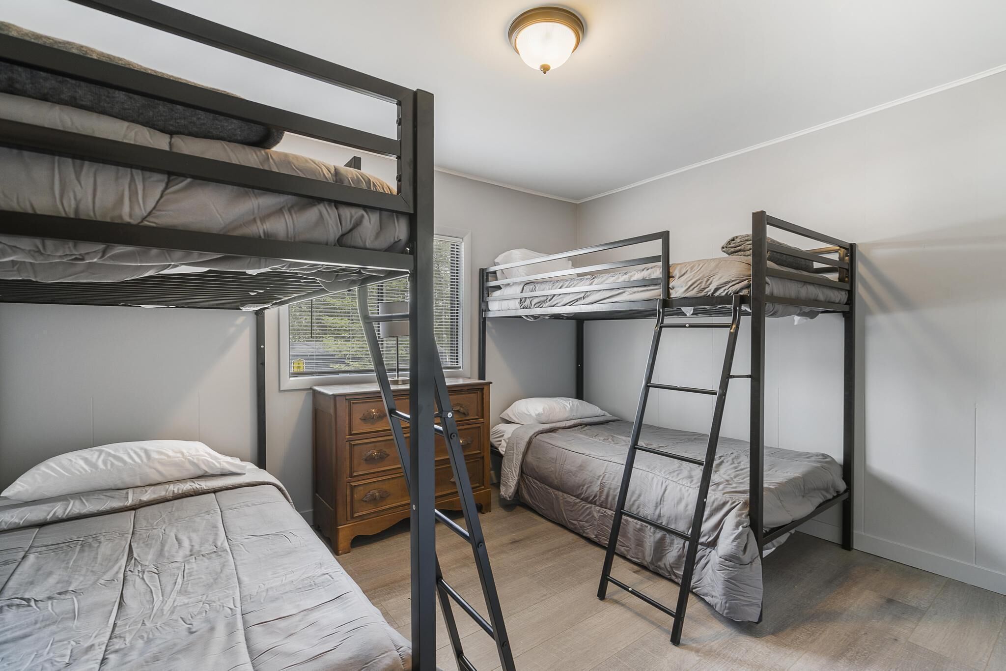 A dormitory room with bunk beds, a wooden dresser, and a window with blinds.