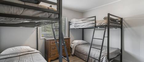 A dormitory room with bunk beds, a wooden dresser, and a window with blinds.