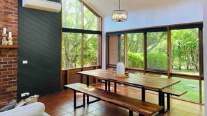 Un comedor moderno con una mesa de madera y bancos, ventanas amplias con vistas a zonas verdes, y una lámpara colgante.