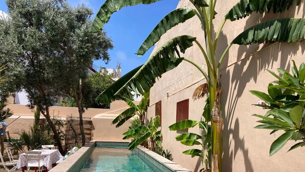 Une piscine à l’eau d’un bleu cristallin, entourée d’une végétation luxuriante et bordée d’un bâtiment de couleur beige.