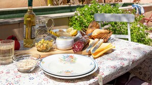 Un espace de restauration en plein air avec une table dressée pour un repas, comprenant du pain, du fromage et une bouteille de vin.