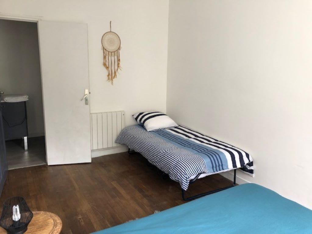 Ein kleines Zimmer mit einem Einzelbett, einer blau-weißen Bettdecke, einem Traumfänger an der Wand und Holzboden.