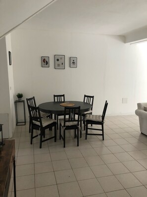 A dining area with a round table surrounded by six chairs, a small side table, and three framed pictures on the wall.