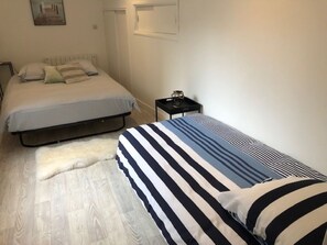A bedroom with two beds, one with a striped bedspread and the other with a plain one. There is a small nightstand with a lamp and a picture frame.