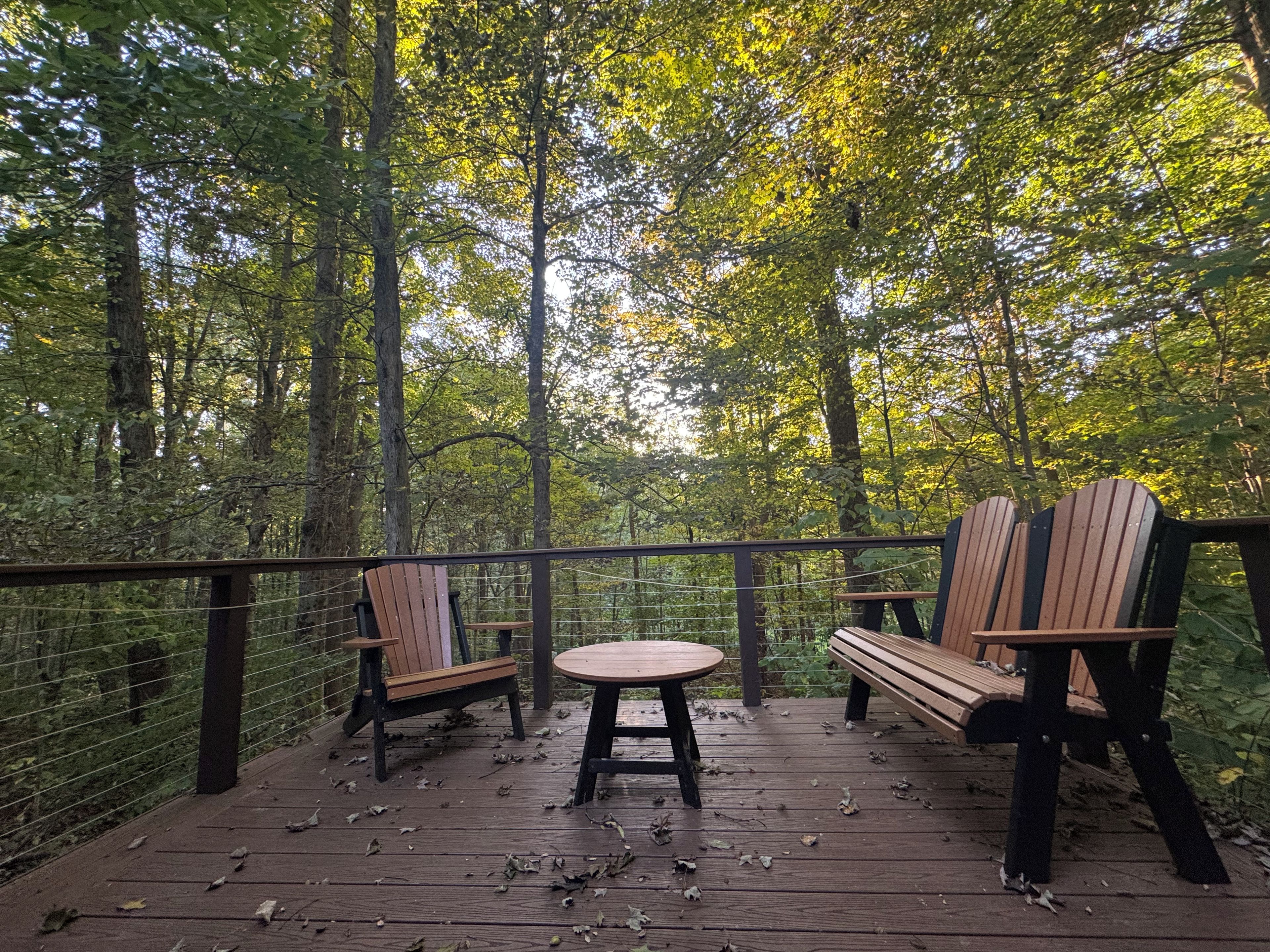Een houten terras met twee Adirondack-stoelen en een kleine ronde tafel, omgeven door bebossing.