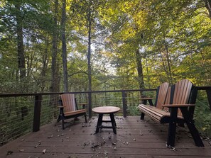 A wooden deck with two Adirondack chairs and a small round table, surrounded by a forested area. - Quiet cottage nestled in the woods (Mount Gilead)