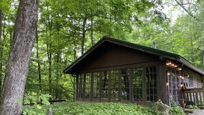 A rustic cabin with large windows and a porch, surrounded by dense forest. - Quiet cottage nestled in the woods (Mount Gilead)