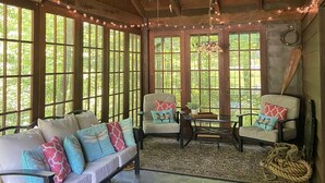 A cozy room with a stone floor, wooden ceiling beams, a ceiling fan, and a large window with a view of greenery. - Quiet cottage nestled in the woods (Mount Gilead)