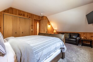 Et soveværelse med seng, træpaneler, en lædersofa, et lille bord og et vægmonteret fjernsyn.