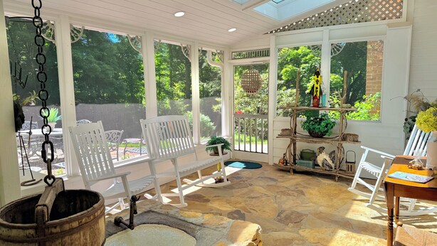A sunlit room with large windows, a stone floor, white furniture, and a wooden barrel.