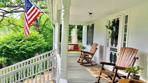 A porch with a white railing, wooden rocking chairs, and an American flag.