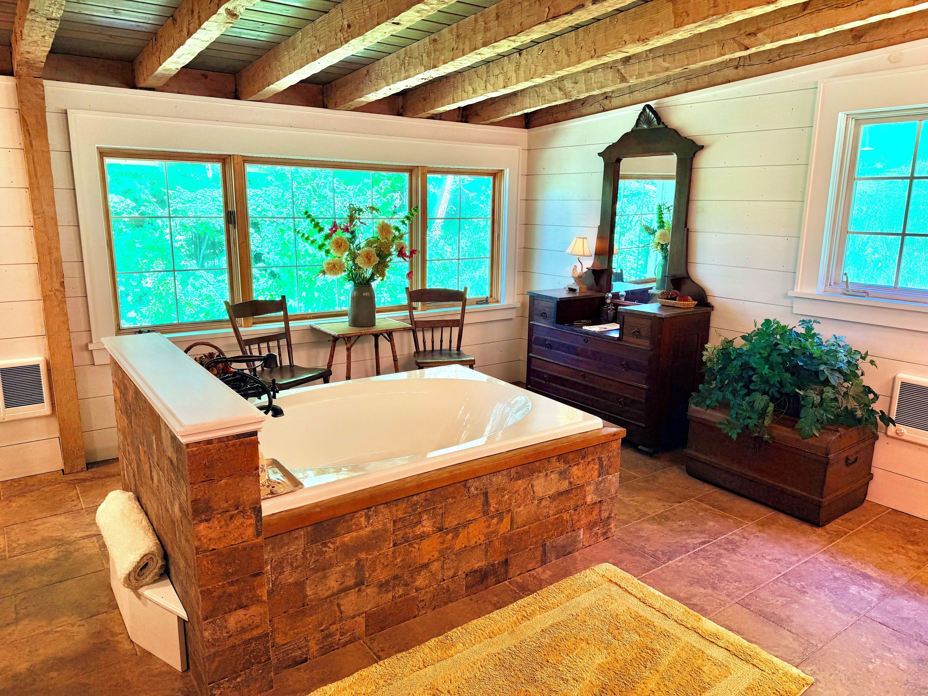 A bathroom with a freestanding bathtub, wooden vanity, and large windows with a view of greenery.