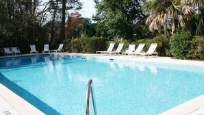 A swimming pool with clear blue water, surrounded by white lounge chairs and lush greenery.