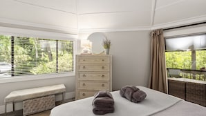 A bedroom with a bed, a dresser, a bench, and a window with blinds.