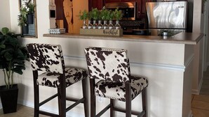 Un coin cuisine agrémenté d’une enseigne de style rustique, de deux tabourets de bar, d’un réfrigérateur et d’un four à micro-ondes.