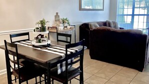 Un coin repas comprenant une table et des chaises, un lustre et une fenêtre avec des stores.