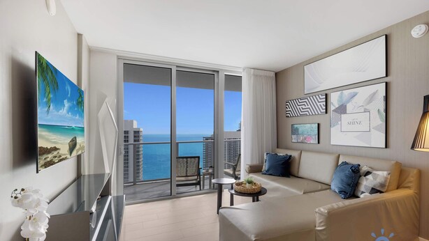 A modern hotel room with a balcony, a sofa, a TV, and artwork on the walls. - High Floor 2BR|2 BA| Resort Fees & Parking Incl. (Hollywood)