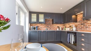 A modern kitchen with dark cabinets, a brick backsplash, and a dining area with a wooden table and chairs.