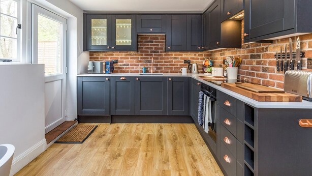 A modern kitchen with dark cabinetry, a brick backsplash, and wooden flooring.