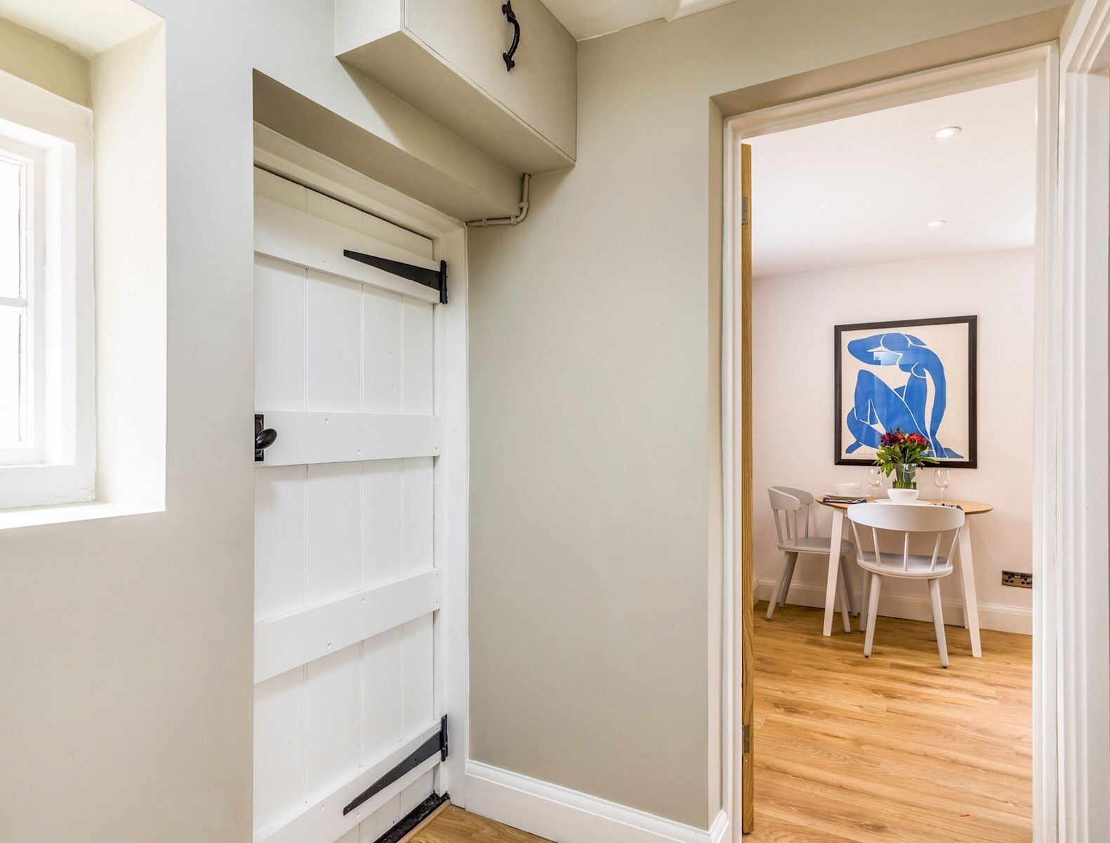 A hallway with a white door, a dining area with a table and chairs, and a blue abstract painting on the wall.
