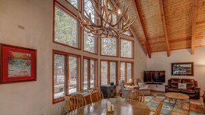 A spacious living room with a high ceiling, large windows, a fireplace, and a television.