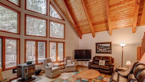 A cozy living room with large windows, a fireplace, leather sofas, and a flat-screen TV.