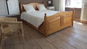 A wooden bed with a white bedspread, a bedside table with a lamp, a wicker chair, and a radiator. - 3 bedroom house (Siaugues-Sainte-Marie)