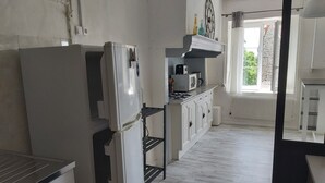 A kitchen with white cabinetry, a refrigerator, a microwave, and a stove. There is a window with curtains and a view of greenery outside. - 3 bedroom house (Siaugues-Sainte-Marie)