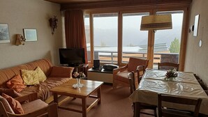 Ein gemütliches Wohnzimmer mit Sofa, Couchtisch, Fernseher und Essbereich mit Stühlen und Tisch.