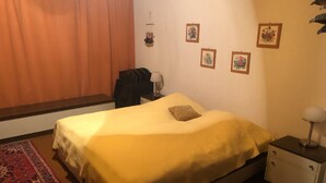 Ein Schlafzimmer mit einem Bett, einem Nachttisch, einem Sessel, einem Schreibtisch und einer Wand mit gerahmten Bildern.