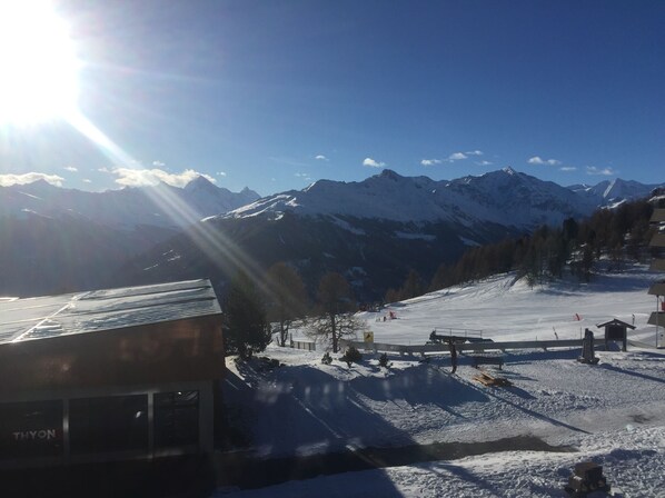 A snowy mountain landscape with a ski slope, a building labeled 'THYON', and distant snow-capped mountains under a clear sky. - Ski in, ski out—straight from bed to the slopes... Live right in the ski resort at 2,000 meters (Thyon)