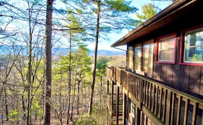 A wooden cabin with a deck overlooking a forested area.