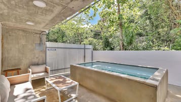 Un área de piscina al aire libre con solárium de hormigón, tumbonas de madera y una valla blanca al fondo.