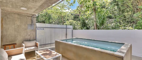 Ein Außenpoolbereich mit einer Betonplattform, Holzliegen und einem weißen Zaun im Hintergrund.