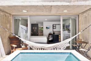 A pool area with a hammock, a bed, a kitchenette, and a bathroom visible through glass doors. - Viento Beach Lodge (Dorado)