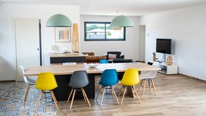A modern kitchen with a dining area, featuring a wooden table, colorful chairs, and pendant lights. - Seaside villa with large pool and terrace (Vendays-Montalivet)
