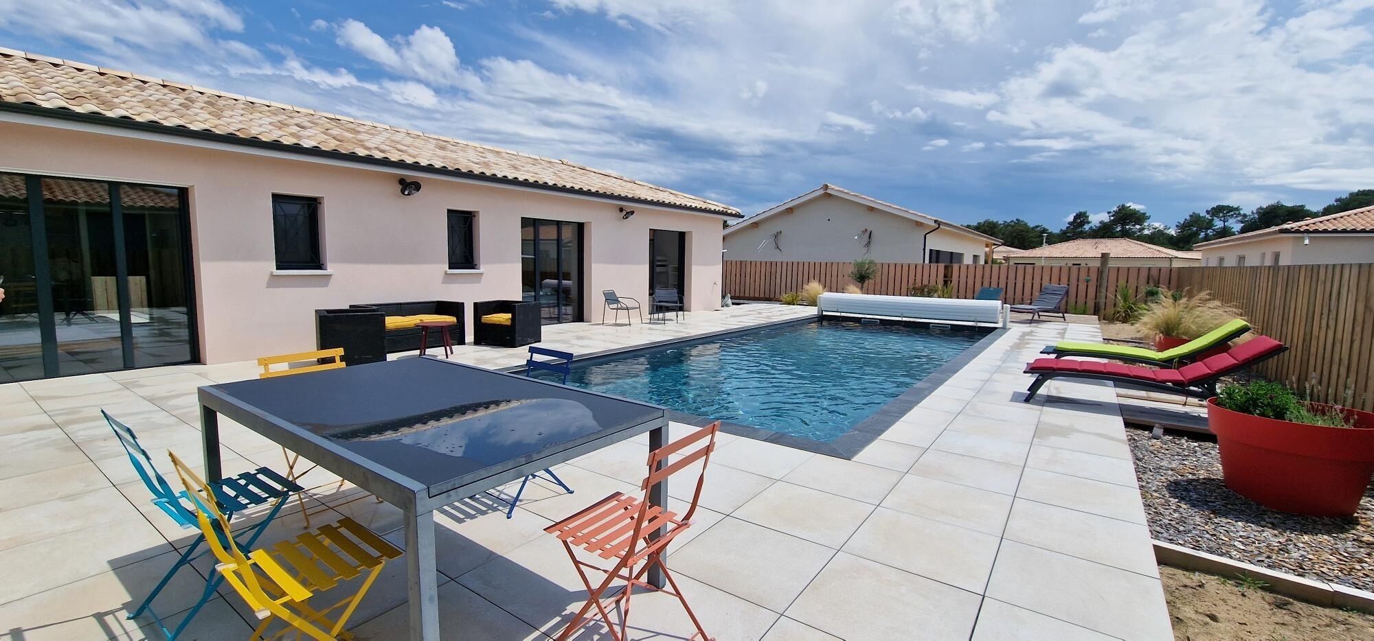 A swimming pool with a tiled deck, outdoor seating, and a wooden fence.