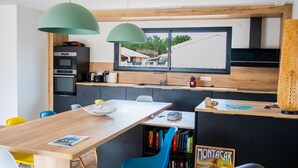 A modern kitchen with a wooden countertop, a built-in oven, and a window overlooking a residential area. - Seaside villa with large pool and terrace (Vendays-Montalivet)