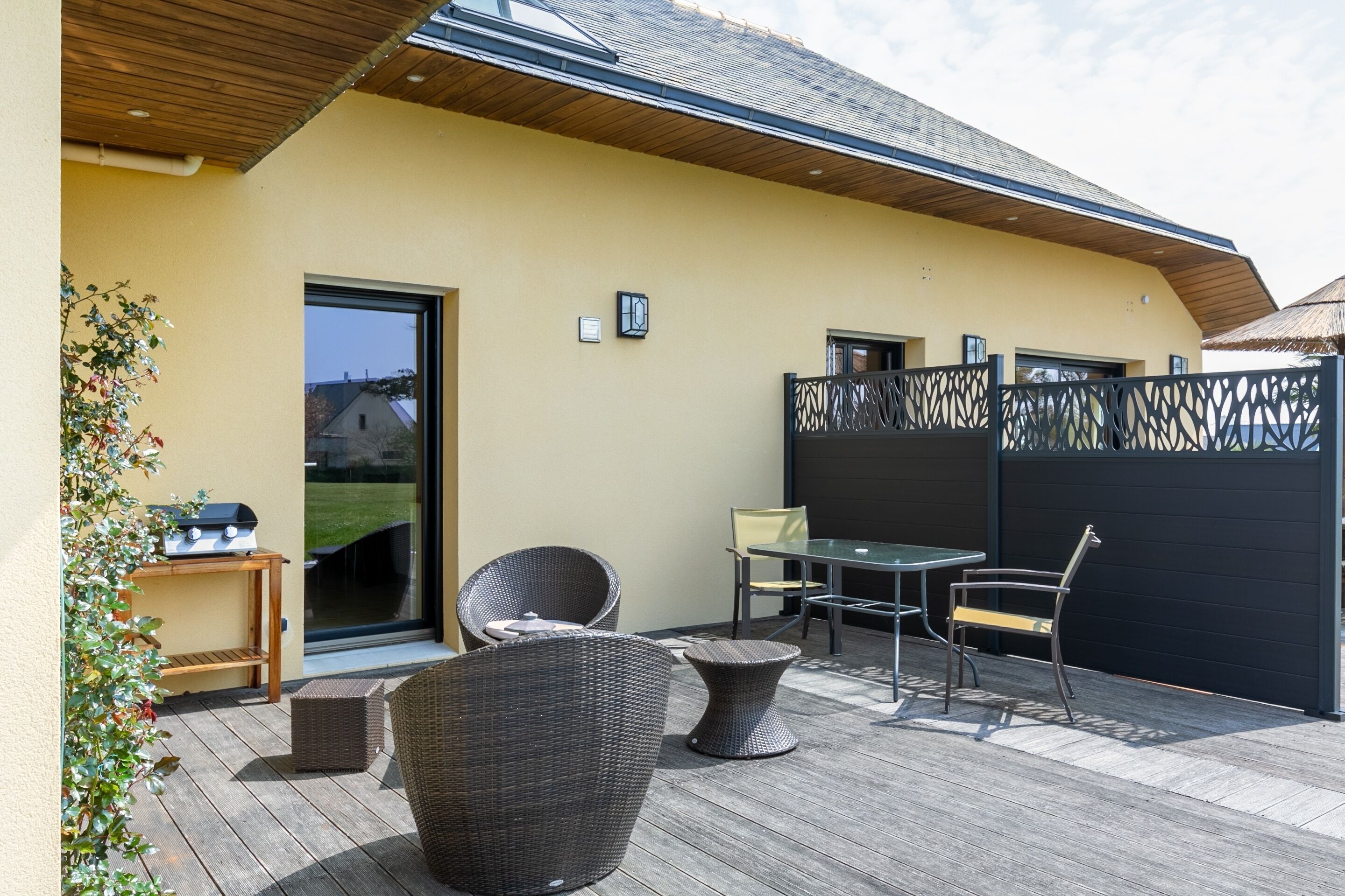 An outdoor patio area with wicker furniture, a grill, and a view of the surrounding landscape.