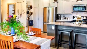 A modern kitchen with stainless steel appliances, wooden chairs, and a dining table set for a meal. - Artisan Boho, Equine Too, Farm Fresh Eggs, Spa, Vino & Views! (Sebastopol)