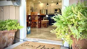 A well-lit entrance with a doormat reading "Our Nest," a wooden dining table with chairs, and potted plants. - Artisan Boho, Equine Too, Farm Fresh Eggs, Spa, Vino & Views! (Sebastopol)