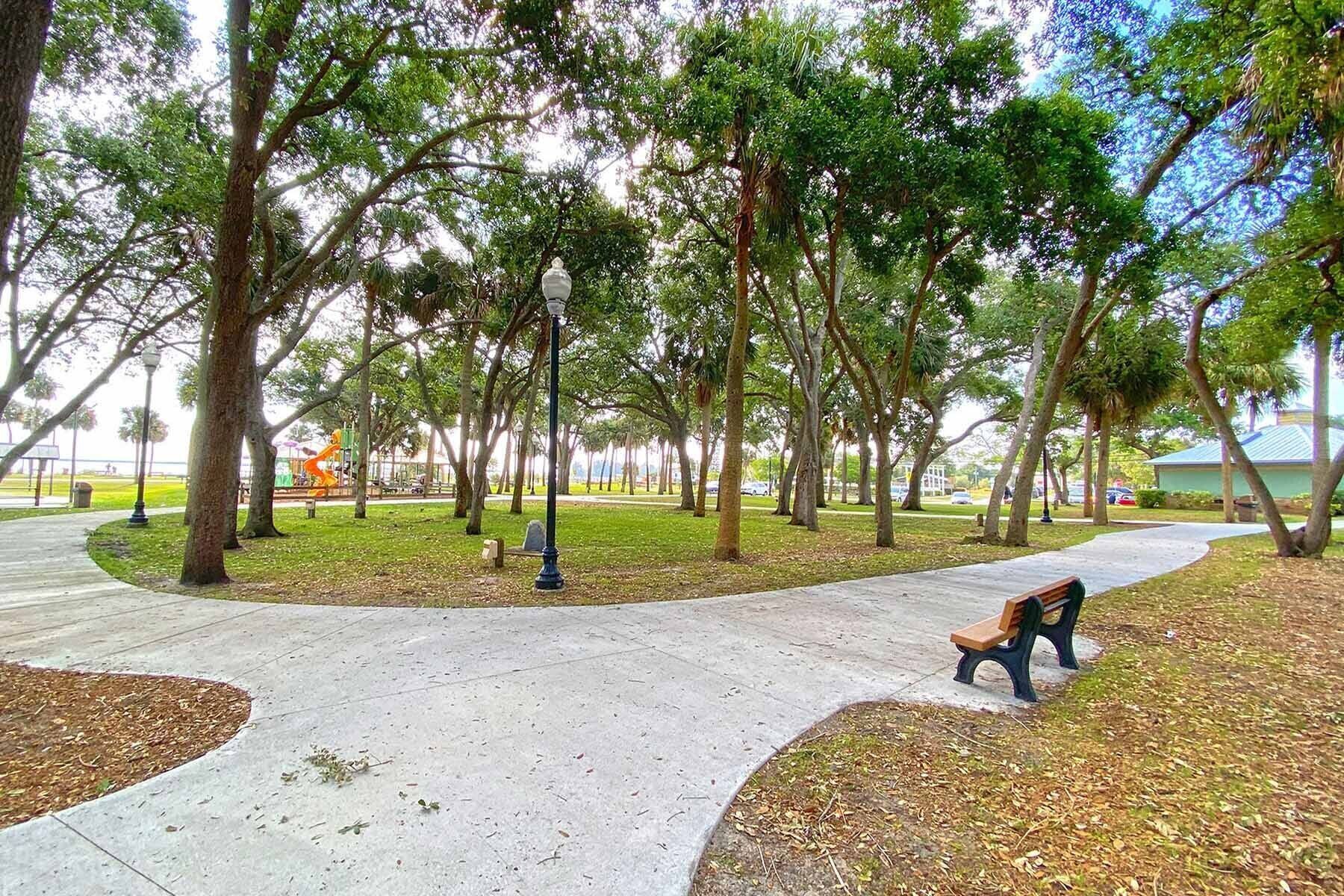 Un parco con un vialetto lastricato, panchine e alberi.