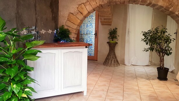 A room with a white cabinet, a potted plant, a tiled floor, and a stone archway. - Character house (PUIMISSON)